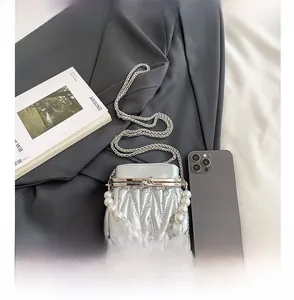 Macro detail of silver pleated mini bag with pearl handle compared to a smartphone