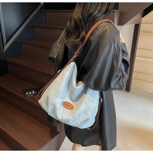 Side view of light blue tote bag with brown leather straps held by a model on stairs