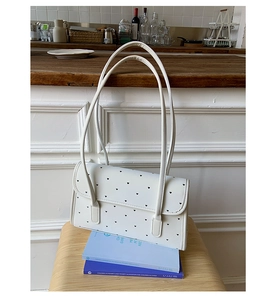 Detailed view of white baguette bag with heart print placed on two books at home