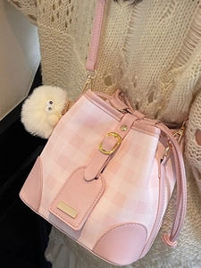 Pink and white checkered bucket bag with plush charm and adjustable strap on a model