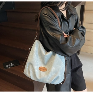 Close-up of gray hobo bag featuring brown leather strap and brand leather patch
