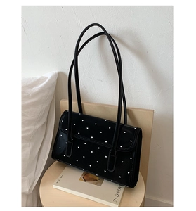 Detailed view of black patent leather underarm bag with white heart pattern and dual straps