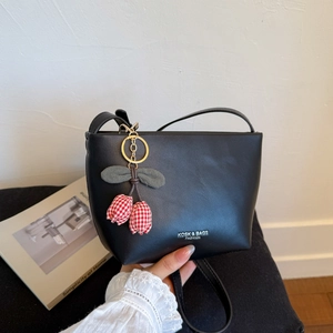 Detailed close-up of a black leather bucket bag with red tulip charm and metal chain