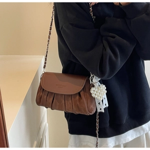 Detail of a brown leather crossbody bag featuring a metal chain strap and pearl heart charm