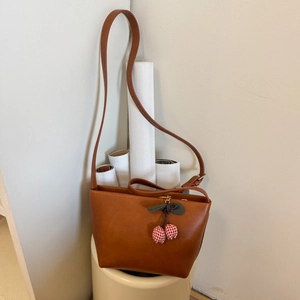 Detailed macro of a brown matte faux leather bucket bag with a fabric cherry pendant