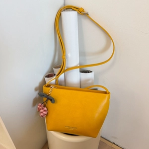 Close-up of yellow PU leather shoulder bag with a stylish cherry charm and text detail