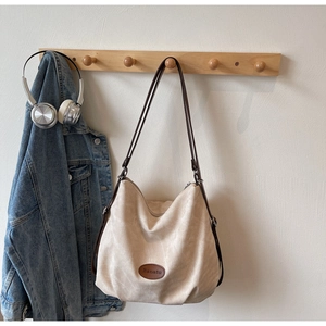 Detail of canvas hobo tote bag featuring brown leather logo patch and shoulder straps