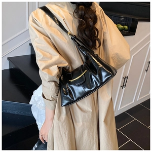 Detail view of glossy black pleated underarm bag featuring a crescent gold metal buckle