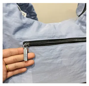 Detailed close-up of the smooth silver metal zipper on a light blue pleated crossbody bag