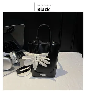 Detail of black leather tote bag featuring a white flower charm and fashion lettering