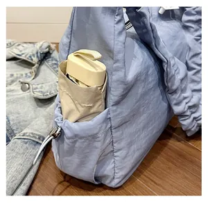 Close-up of sky blue pleated tote bag side pocket holding a beige folding umbrella