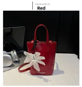 Detail of red glossy leather bucket bag with gold lettering and white flower charm