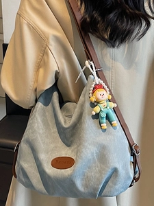 Minimalist light blue canvas tote bag with brown leather straps and cartoon doll charm