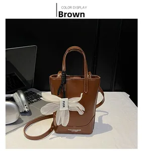 Detailed view of a brown leather tote bag with white flower charm on a white desk setup