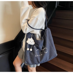 Vue latérale d'un grand sac cabas en jean avec lettres imprimées et un charm en peluche