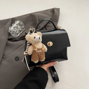 Detail of black glossy leather handbag featuring a gold twist lock and a cute bear charm