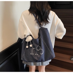 Détail du sac cabas en jean bleu avec coutures blanches et accessoire nuage en peluche