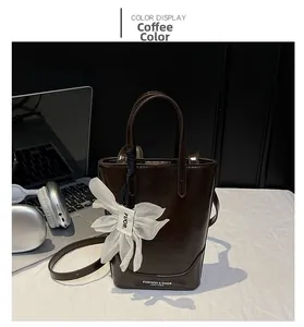 Detail of coffee brown leather bucket bag featuring white bow charm and adjustable strap