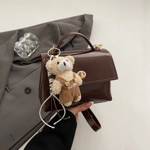 Detail of dark brown glossy leather handbag featuring golden twist lock and a cute plush bear