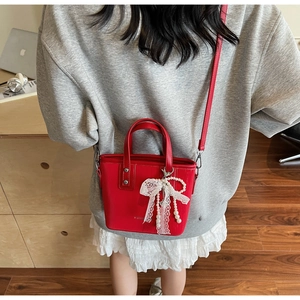 Detail of red textured bucket bag featuring white lace bow and pearl charm ornament
