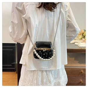 Detail of a black pleated mini bag with a pearl handle and chain strap on a model