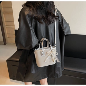 Close-up of a cream mini bucket bag featuring a lace bow and pearl pendant detail