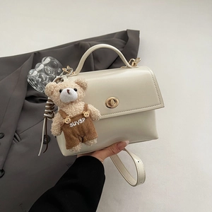 Detail of white square handbag with golden turn-lock and a plush bear charm on side