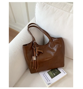Close-up of caramel brown leather tote bag with T-shaped pendant and tassel on white sofa