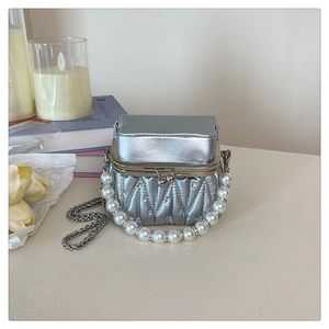 Detail of silver quilted mini bag with pearl handle and metal chain on a desktop