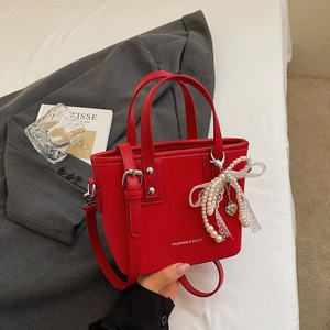Close-up of red bucket bag featuring vertical texture and pearl lace bow charm