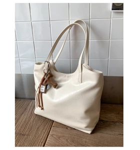 Detail of cream leather tote bag featuring brown tassel and large T-shaped charm pendant