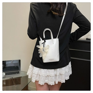 Detail view of a white leather mini bucket bag featuring a delicate mesh flower charm