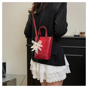 Chic red leather mini tote bag with a floral charm accessory worn in a modern room
