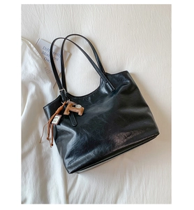 Close-up of black tote bag with polished leather texture and brown H-pendant detail