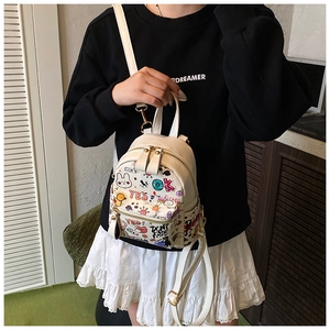 Detail view of mini white backpack featuring colorful cartoon graffiti and gold zippers