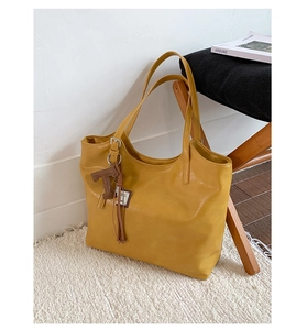 Detail of yellow PU leather tote bag featuring a brown T-shaped tassel charm decoration