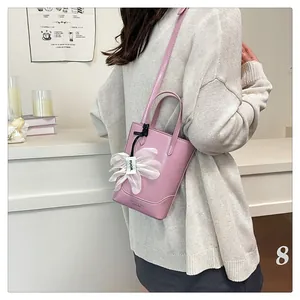Pink PU leather tote bag with flower pendant shown on a model in a minimalist setting