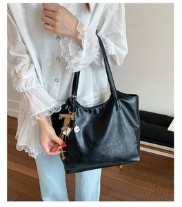 Detail of black tote bag featuring a leather matte finish and brown T-letter charm