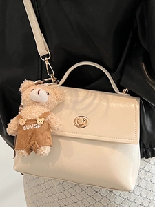 Chic beige glossy leather handbag for women featuring a cute teddy bear charm detail