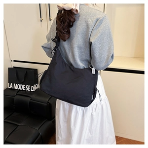 Detail view of a large black nylon crossbody bag with pleated texture and wide strap on model