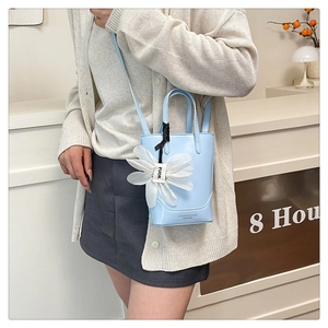 Detail view of light blue leather tote bag with white silk flower charm and shoulder strap