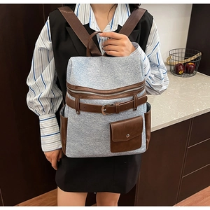 Detail of the large-capacity backpack showing grey denim texture and brown leather accents