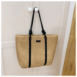 Detail of hand-woven straw tote with black rope handles hanging on a white cabinet