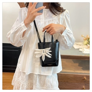 Close-up of black leather tote bag with gold lettering and white flower petal charm