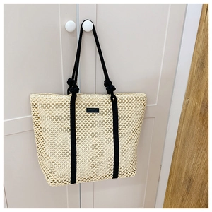 Detail of woven straw tote bag with black rope handles and rectangular leather patch