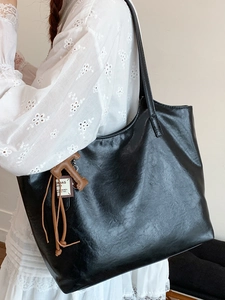 Minimalist black tote bag with vintage leather texture and letter charm accessory