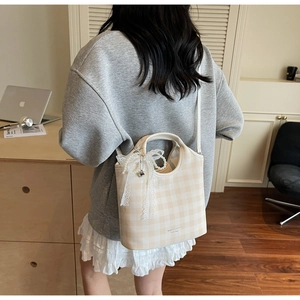 Détail d'un sac à carreaux beige avec nœud en dentelle, perles et pendentif cœur