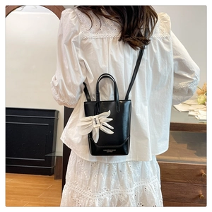 Detail view of black leather tote bag with white floral charm and logo lettering