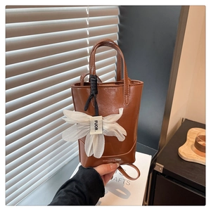 Close-up of brown vintage tote bag featuring a white gauze flower and black ribbon accent
