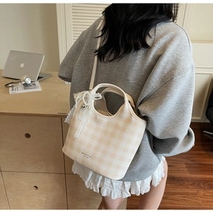 Détail du sac cabas à carreaux avec un nœud décoratif en dentelle et perles sur l'anse